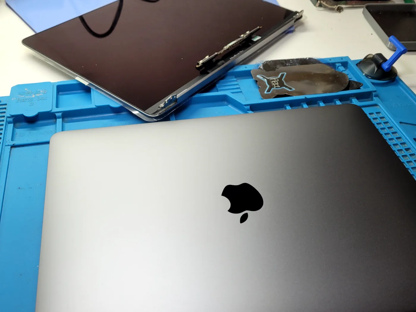Conjunto de pantalla completo retirado de un MacBook Pro A2289 sobre la mesa del taller, junto al equipo cerrado