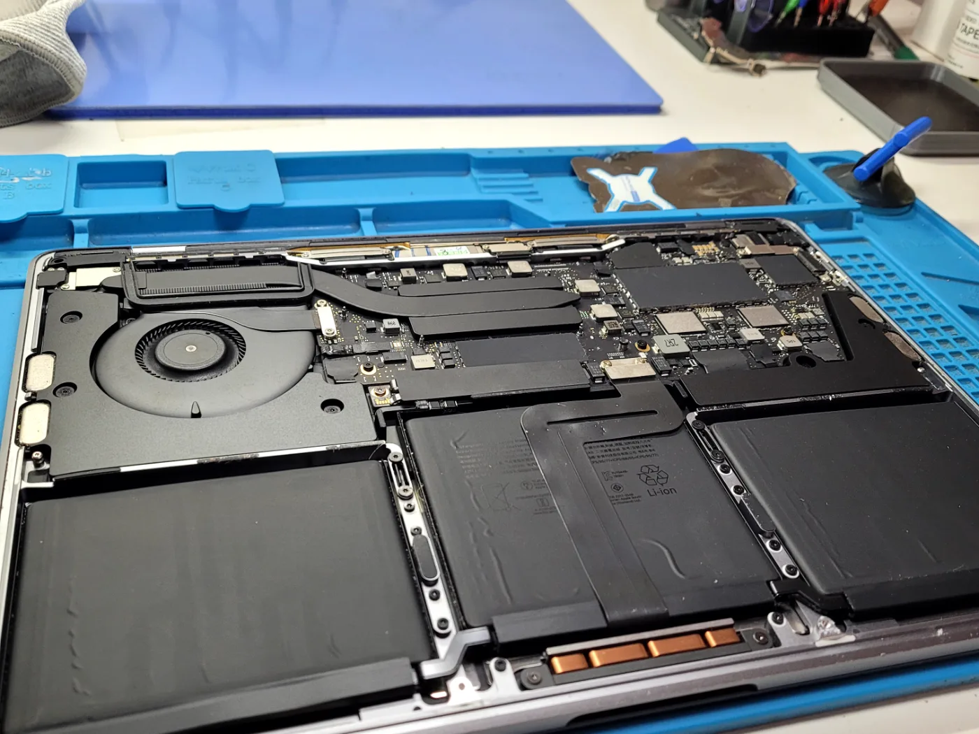 MacBook Pro abierto en el banco del taller, con el ventilador, la placa y la batería a la vista